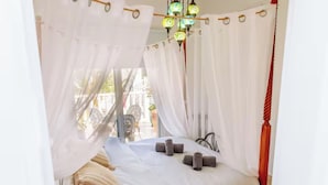 Ein Bett mit weißer Bettwäsche, einem Baldachin und einer Kristallleuchtre.'