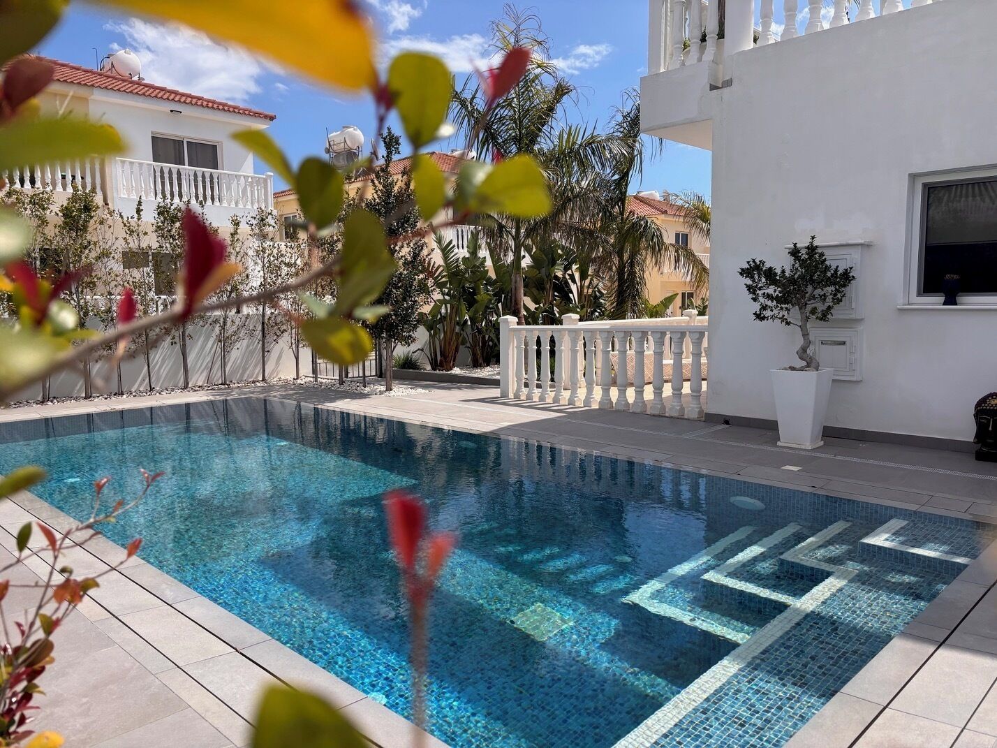 Une piscine à l’eau d’un bleu cristallin, entourée d’un bâtiment blanc doté de balcons et d’une clôture blanche.