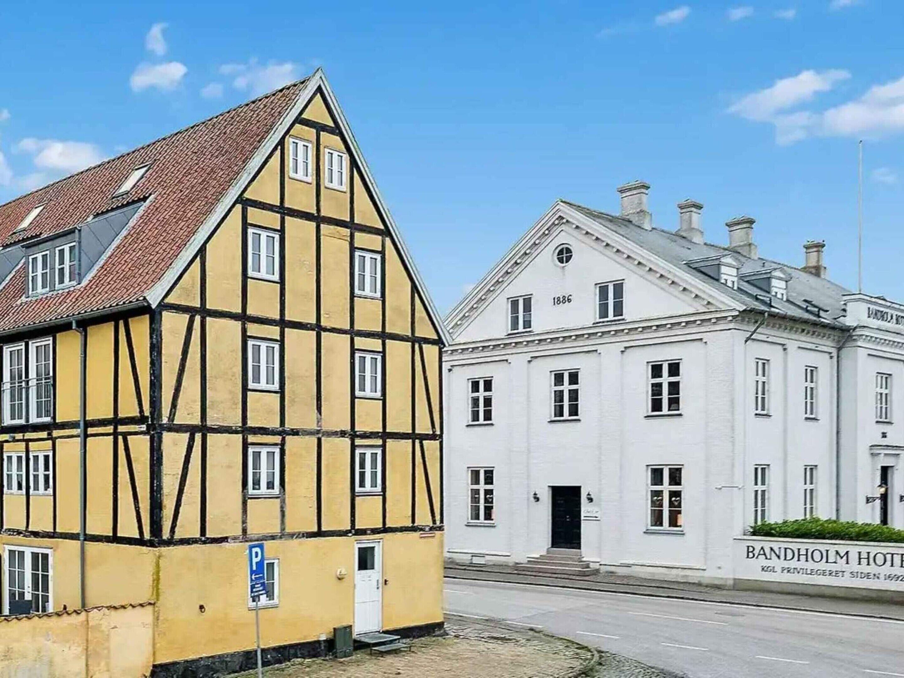 A traditional yellow building with a white facade, a sign for the Bandholm Hotel, and a clear blue sky.
