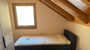 A small, single-bed room with a sloped ceiling and a window.