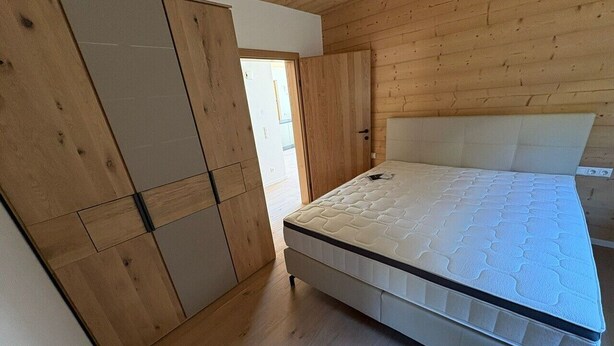 A bedroom with a wooden ceiling, a bed, and a wardrobe.