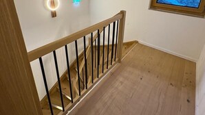 A wooden staircase with a handrail, a small window with a view, and two wall-mounted light fixtures.