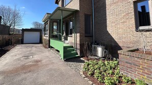 A residential building with a garage, a covered porch, and a brick exterior. - Stylish, Sustainable Apartment in Bree (Bree)