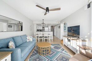 Ein modernes Wohnzimmer mit blauem Sofa, Essbereich, Küche und Deckenventilator.