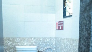 Ein Badezimmer mit Toilette, einem blauen Eimer und einem Wandarmaturen-Wasserhahn.