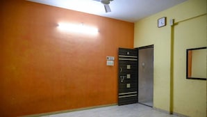 Ein Zimmer mit orangefarbenen Wänden, Fliesenboden, einer Tür mit Sicherheitsschloss, einem Deckenventilator und einer Wanduhr.