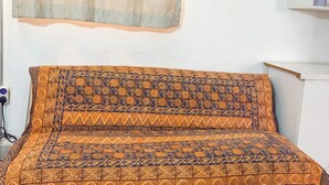 Sängyssä on kuviollinen päiväpeite, seinälle on kiinnitetty hylly ja ikkunassa on läpikuultava verho.