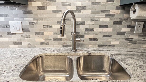 Una cocina con un lavamanos doble de acero inoxidable, salpicadero de azulejos y encimera.