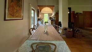 Uma sala de jantar com uma mesa comprida, cadeiras, um lustre e um quadro na parede.