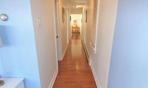 A narrow hallway with wooden flooring, white walls, and a door on the left.