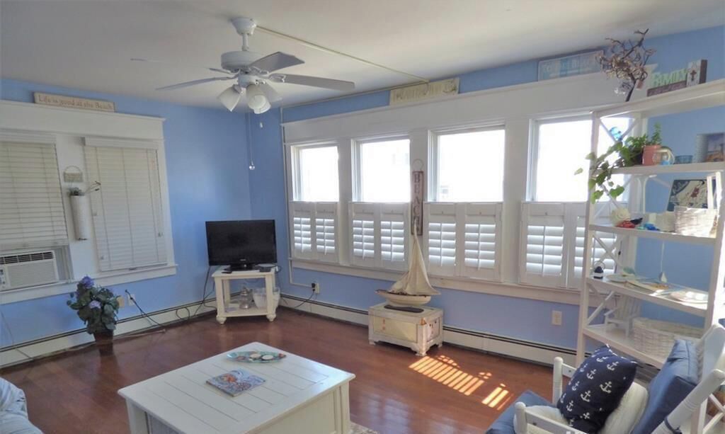 A living room with a ceiling fan, a television, a white coffee table, and a bookshelf.