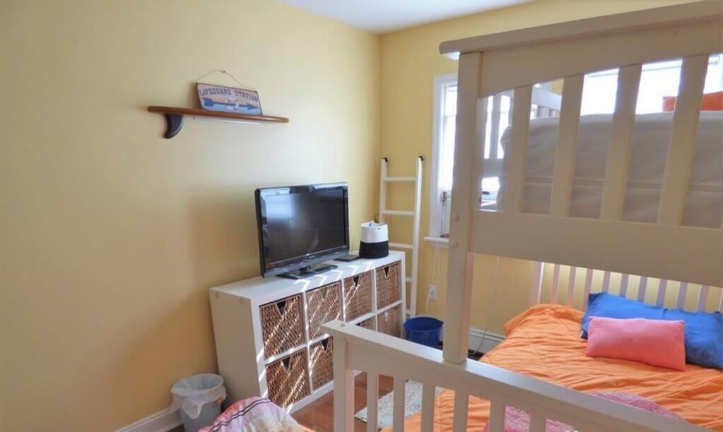 A bedroom with a bunk bed, a television on a white cabinet, a ladder, and a shelf with a lifeguard sign.