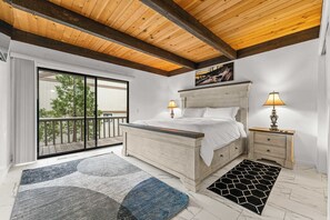 Quarto com uma cama grande, duas mesas de cabeceira, varanda e teto de madeira.