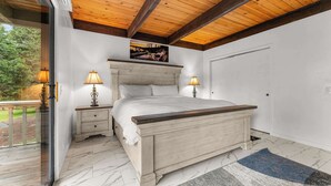 Une chambre avec un plafond en bois, un lit doté d’une tête de lit, deux lampes de chevet, une porte et une vue sur la verdure à l’extérieur.
