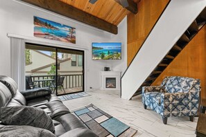 Uma sala de estar com sofá, poltrona estampada, lareira e televisão na parede.