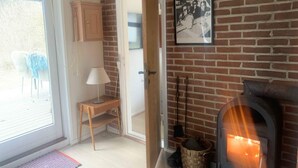 A room with a brick wall, a fireplace, a door leading to another room, a small wooden desk, and a chair.