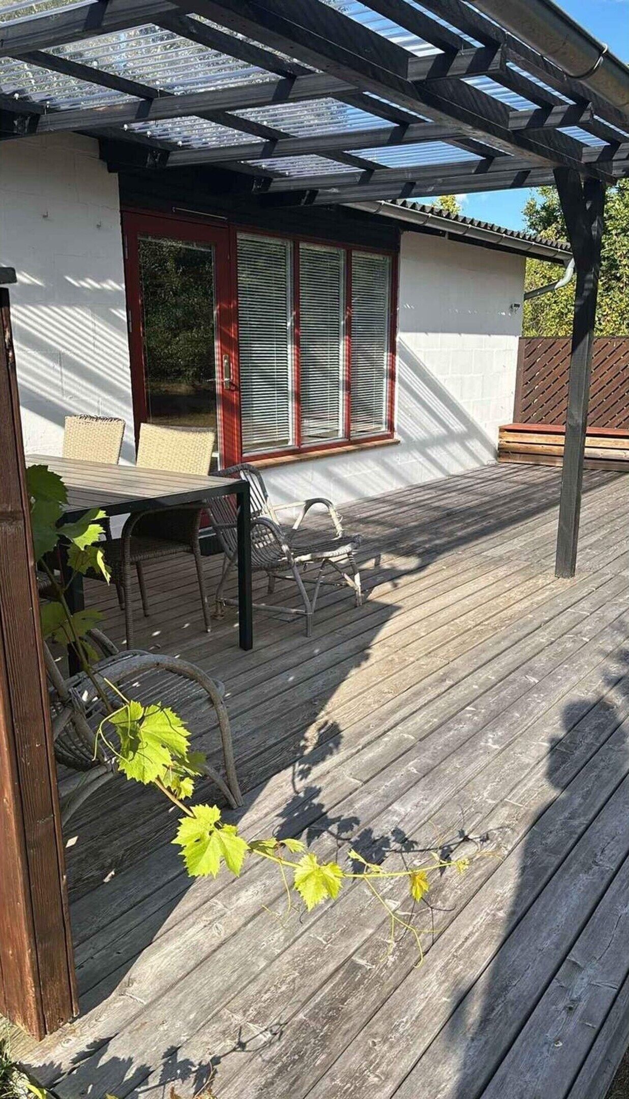 Une terrasse extérieure couverte, agréée d’une pergola, d’une table et de chaises.