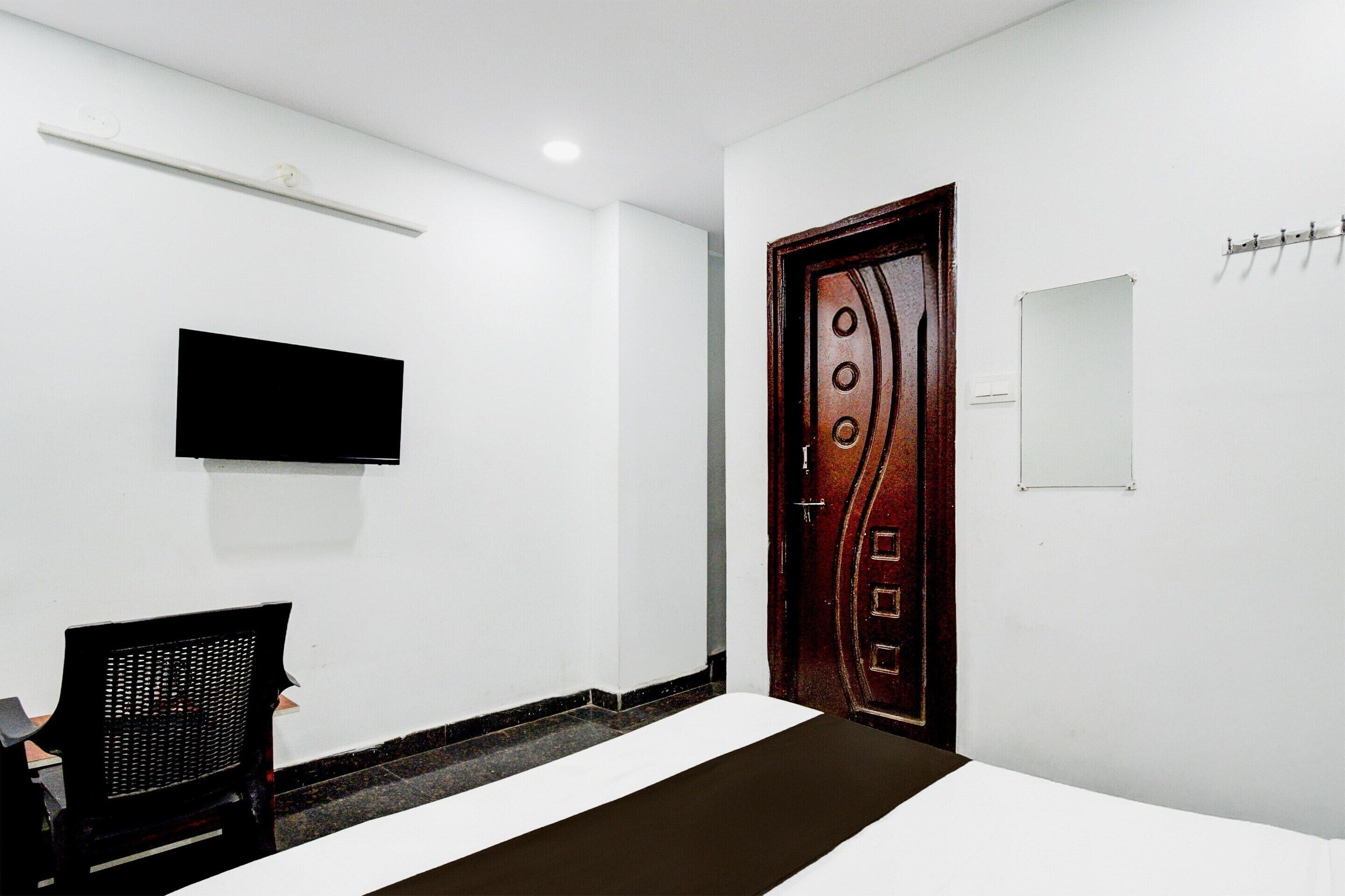 Una stanza con un letto, una televisione a muro, una porta in legno e un appendiabiti.