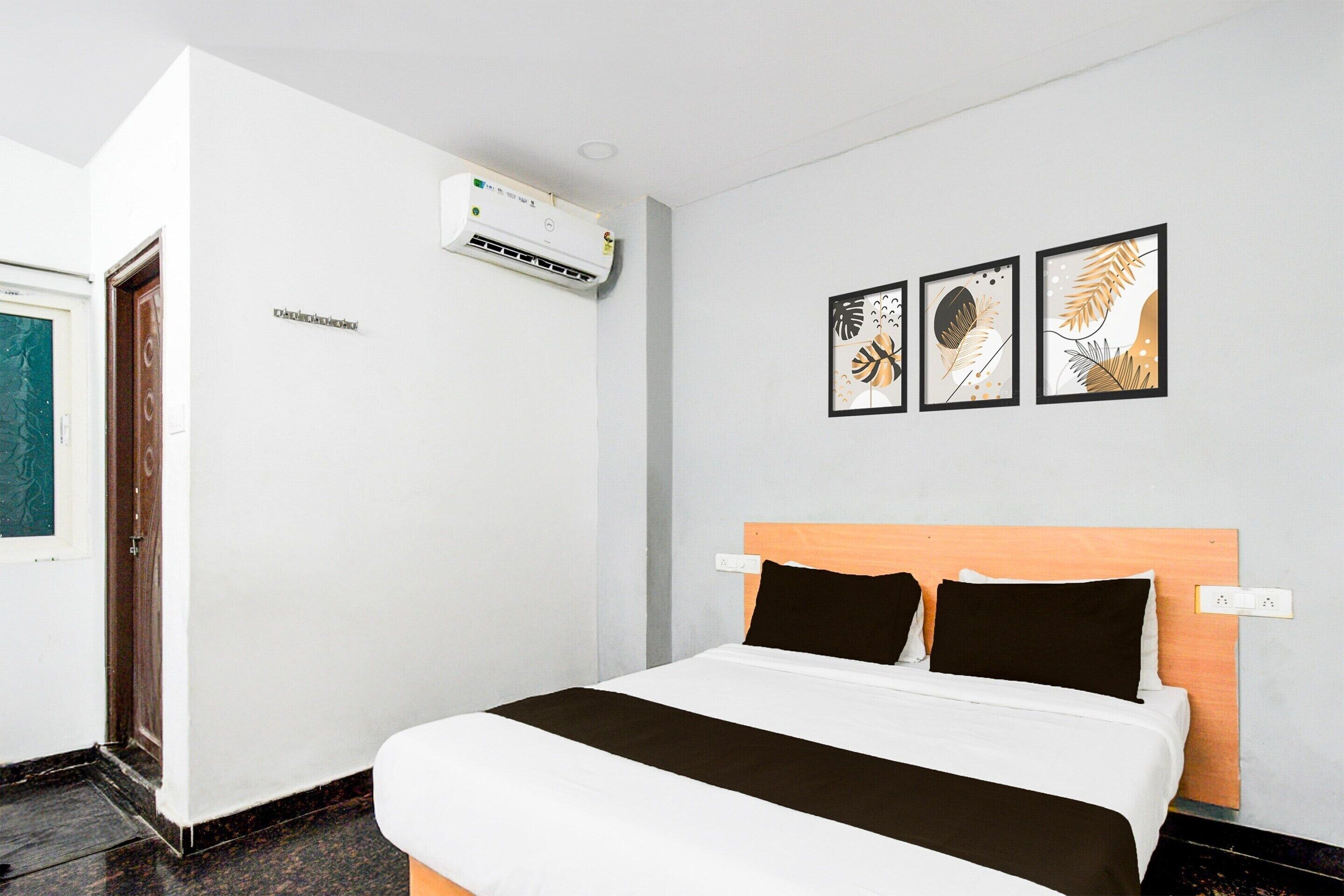 A hotel room with a bed, a wall-mounted air conditioner, and three framed leaf artworks.