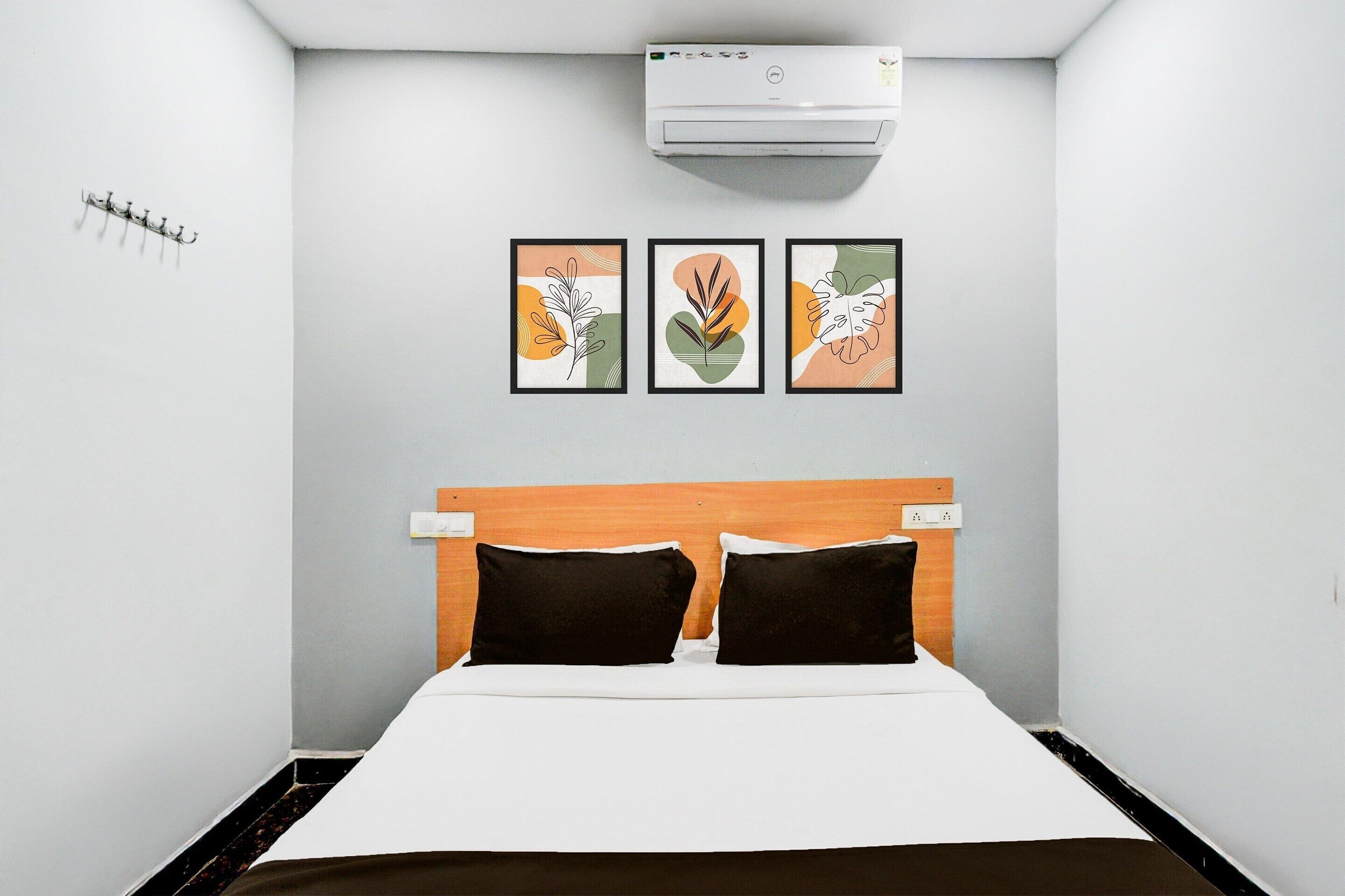 Una habitación pequeña y limpia con cama, aire acondicionado de pared y tres láminas con motivos de hojas.