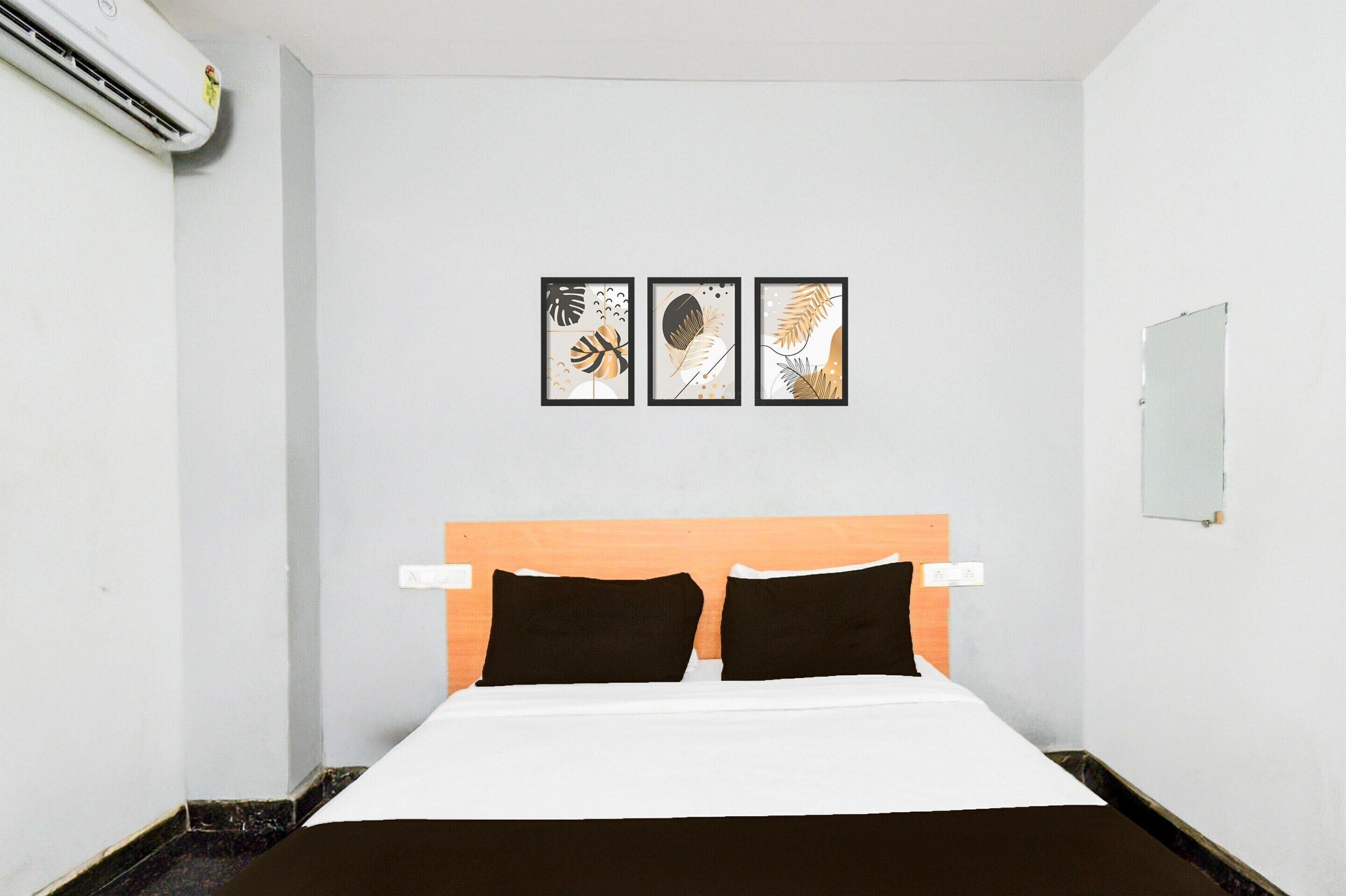 A hotel room with a bed, a headboard, a wall-mounted air conditioner, and three framed leaf artworks.