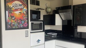 A compact kitchen with white cabinets, a microwave, a small refrigerator, and a globe on the wall. - Sea view apartment facing the beach (Clohars-Carnoët)