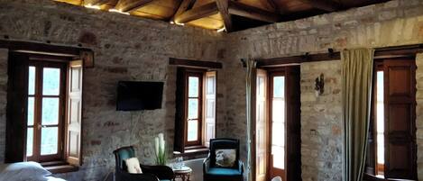 Una habitación rústica con paredes de piedra, vigas de madera, dos camas, una silla, una mesa y un televisor.