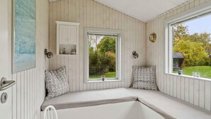 Ein Zimmer mit einer eingebauten Bank, zwei Fenstern, einem an der Wand befestigten Regal und einer Tür.