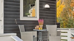 Eine Holzhütte mit einem Fenster, zwei Korbstühlen, einem kleinen Tisch mit Topfpflanzen und einem Geländer.