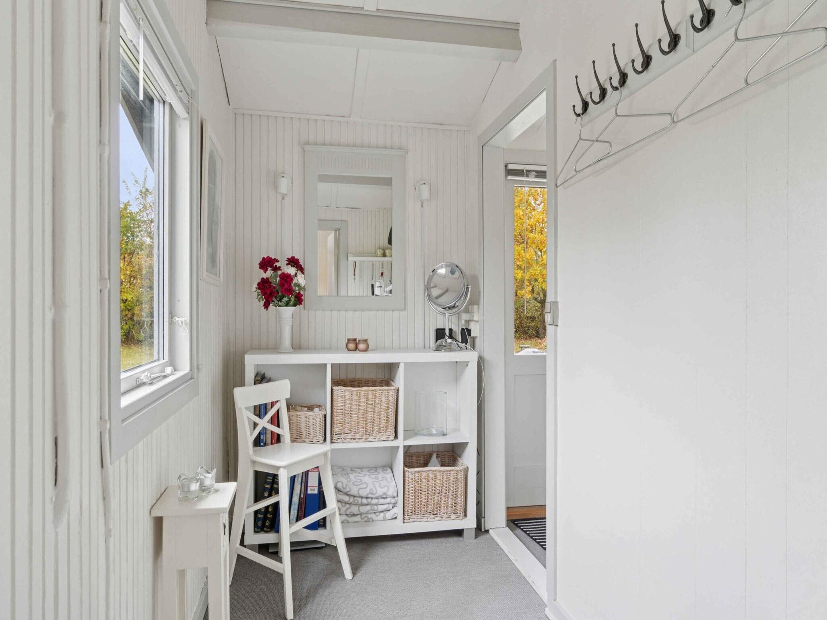 A white room with a vanity, a chair, a mirror, and shelves with baskets.