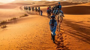 Paisaje desértico con dunas de arena y un grupo de personas montadas en camellos.