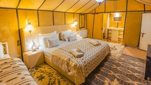 Habitación con tienda de campaña, cama, mesitas de noche, lámpara colgante y baño con lavabo y espejo.