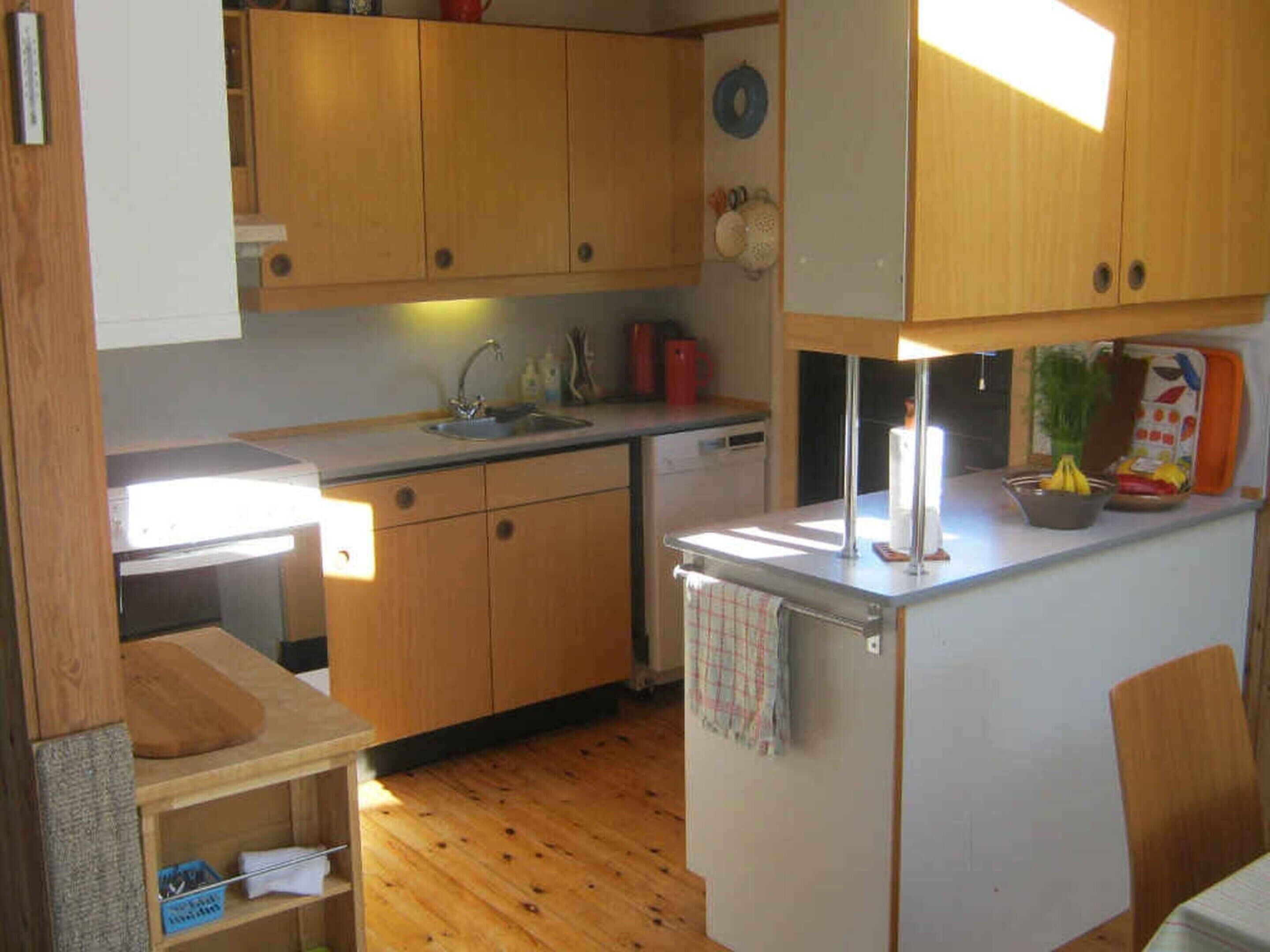 Una cocina compacta con armarios de madera, un lavamanos, un refrigerador pequeño y una encimera con diversos objetos.