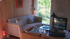 A living room with a sofa, a small table, a fire extinguisher, and a view of greenery outside. - 4 Star Holiday Home in Glesborg (Glesborg)