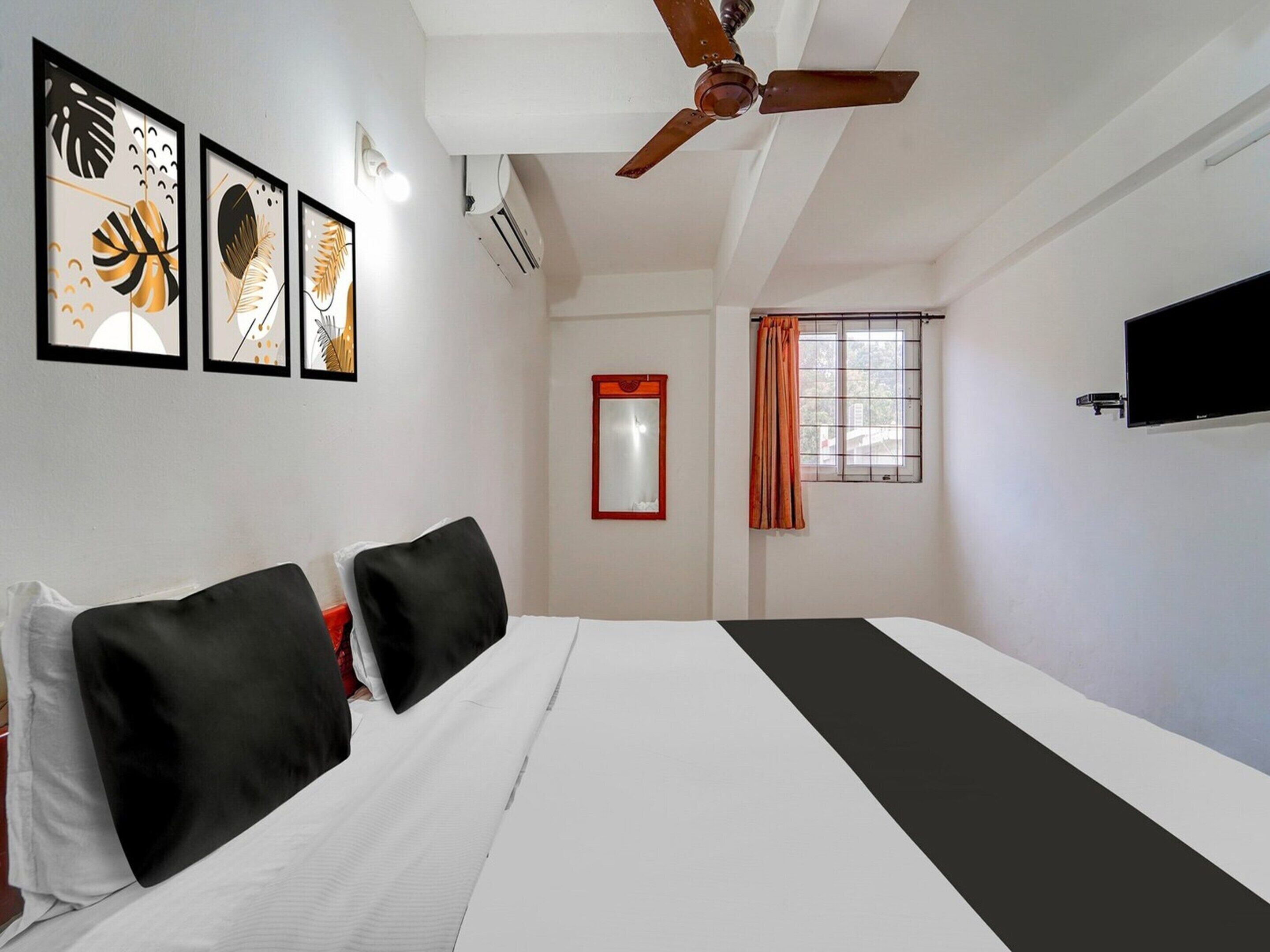 A hotel room with a bed, a ceiling fan, a TV, and artwork on the wall.
