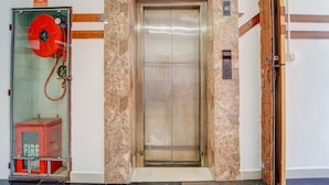 An elevator with a marble wall, a fire extinguisher, and a fire alarm sign. - Classic With Balcony Olive Residency (Kottayam)