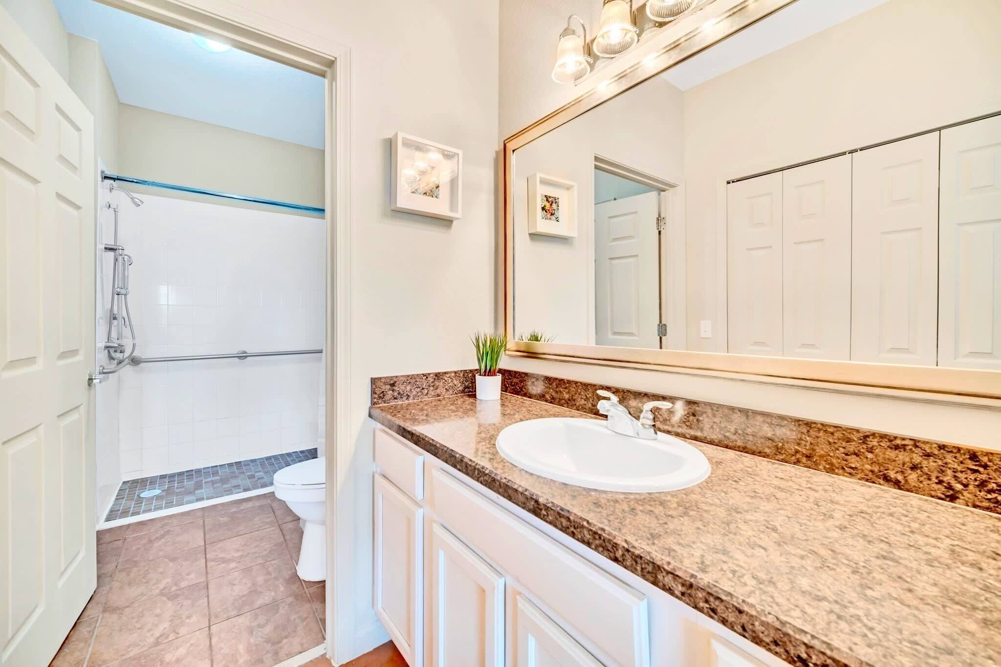 A bathroom with a shower, toilet, sink, and a large mirror.