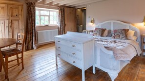 Ein Schlafzimmer mit Holzboden, einem weißen Schminktisch, einem Bett mit Baldachin und einem Fenster mit Vorhängen.