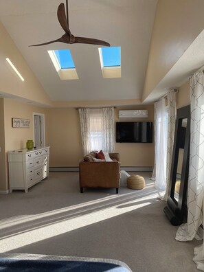 Une pièce avec un ventilateur de plafond, un canapé, un téléviseur et une fenêtre avec des rideaux.