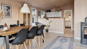 A modern interior with a wooden dining table, black chairs, a hanging light fixture, and a kitchen area with a stove. - 4 Star Holiday Home in Slagelse (Slagelse)