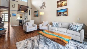 Ein geräumiges Wohnzimmer mit einer Couch, zwei Sesseln, einem Couchtisch und einem Essbereich. Im Hintergrund ist eine Küche zu sehen.