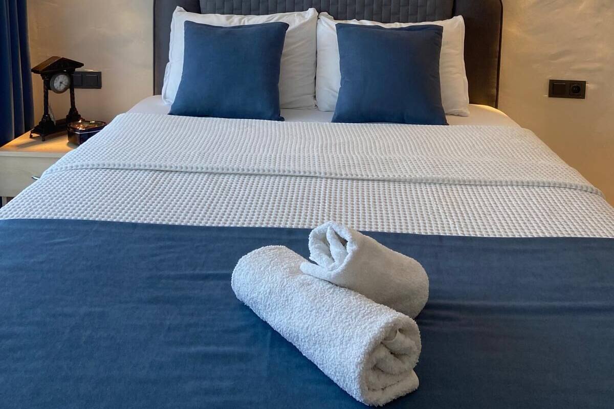 A neatly made bed with a blue and white duvet, two pillows, and a rolled white towel.