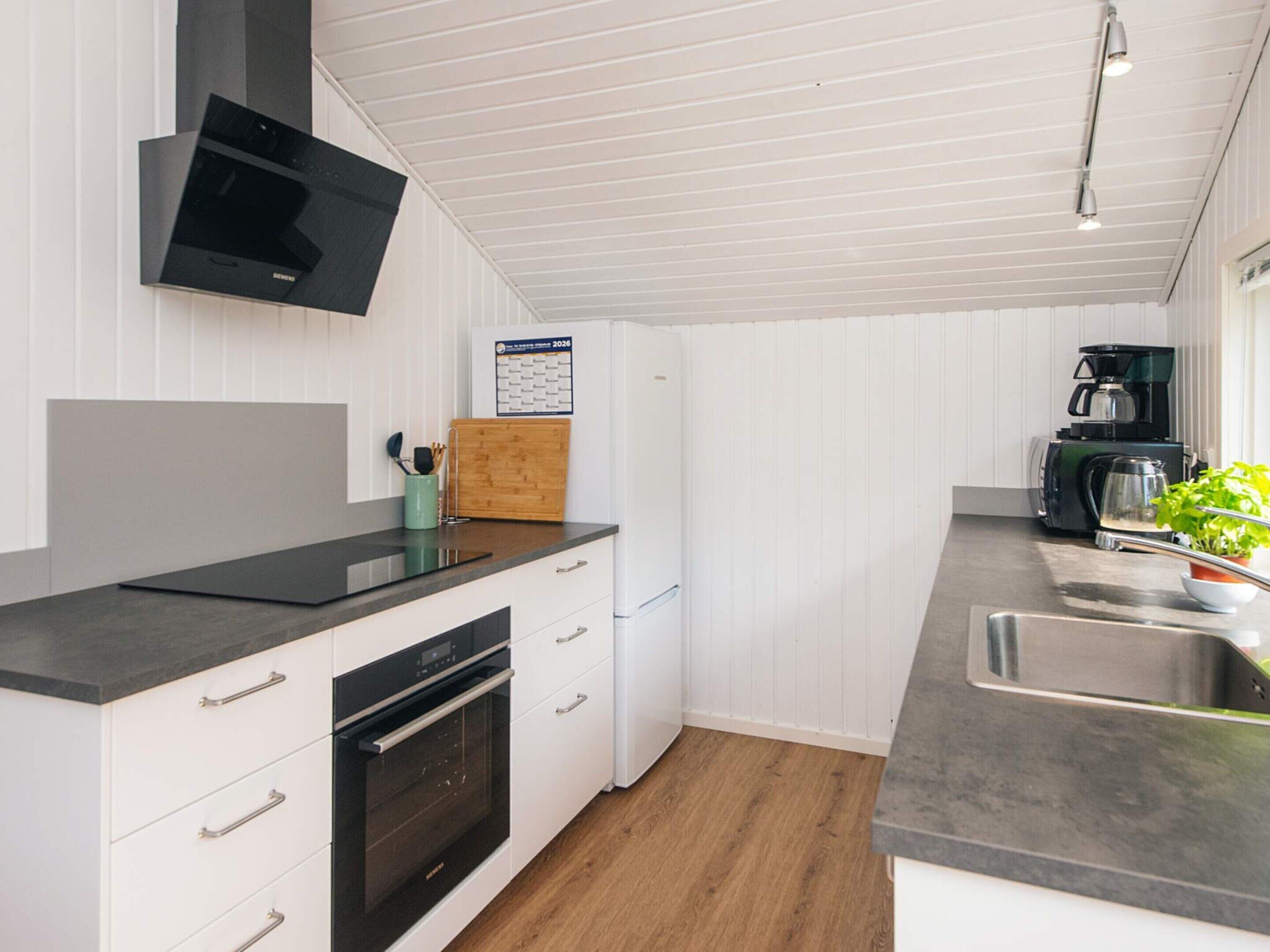 A modern kitchen with white cabinetry, a built-in oven, a microwave, and a coffee maker.