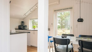 Een moderne keuken met witte kasten, een eethoek met een tafel en stoelen, en een groot raam met uitzicht op de omgeving.