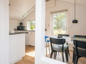 Eine moderne Küche mit weißen Schränken, ein Essbereich mit Tisch und Stühlen sowie ein großes Fenster mit Blick ins Freie.