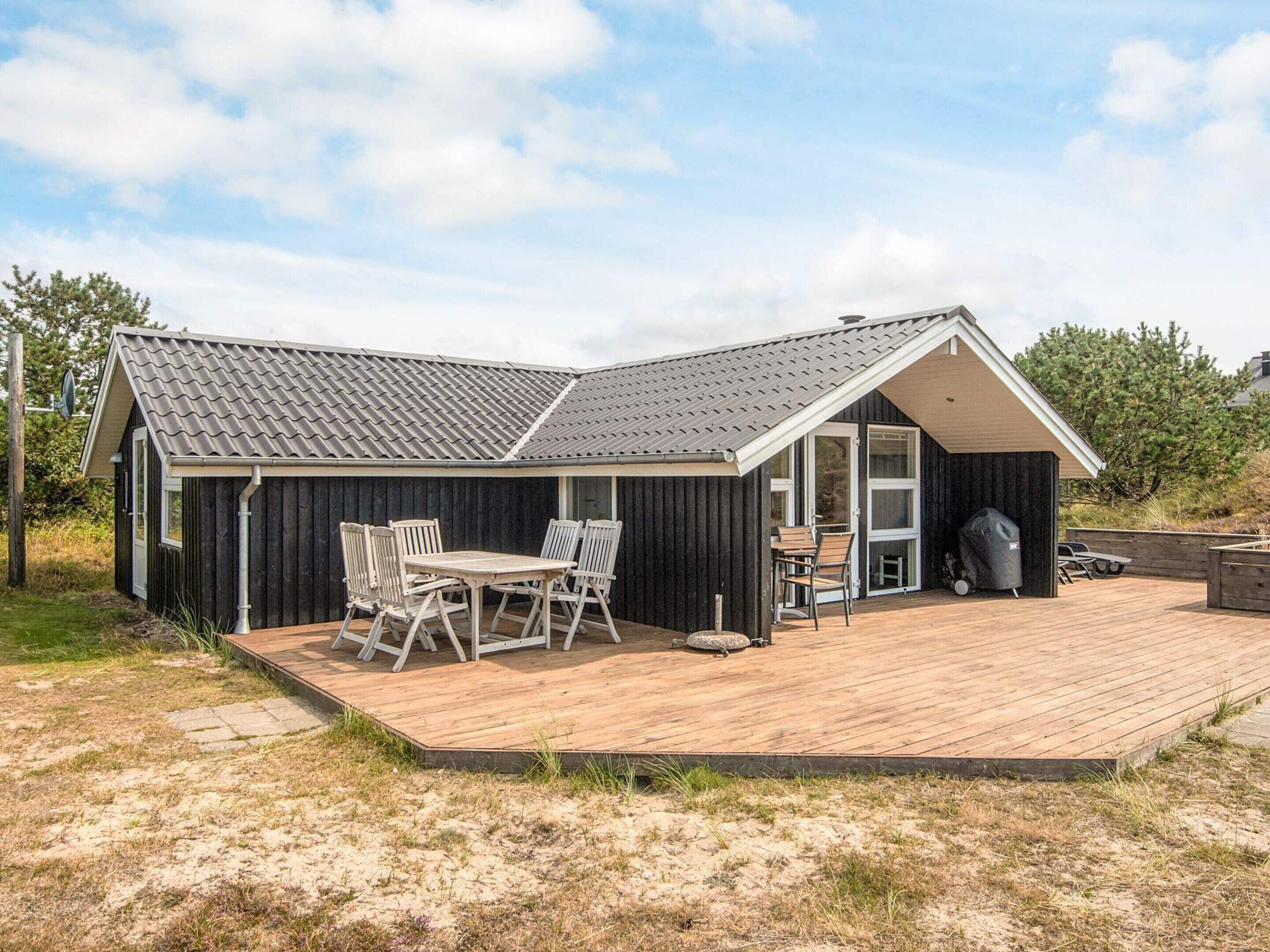 Une maison moderne dotée d’une terrasse en bois, d’un coin repas avec des chaises et d’un garage avec un porche abrité.