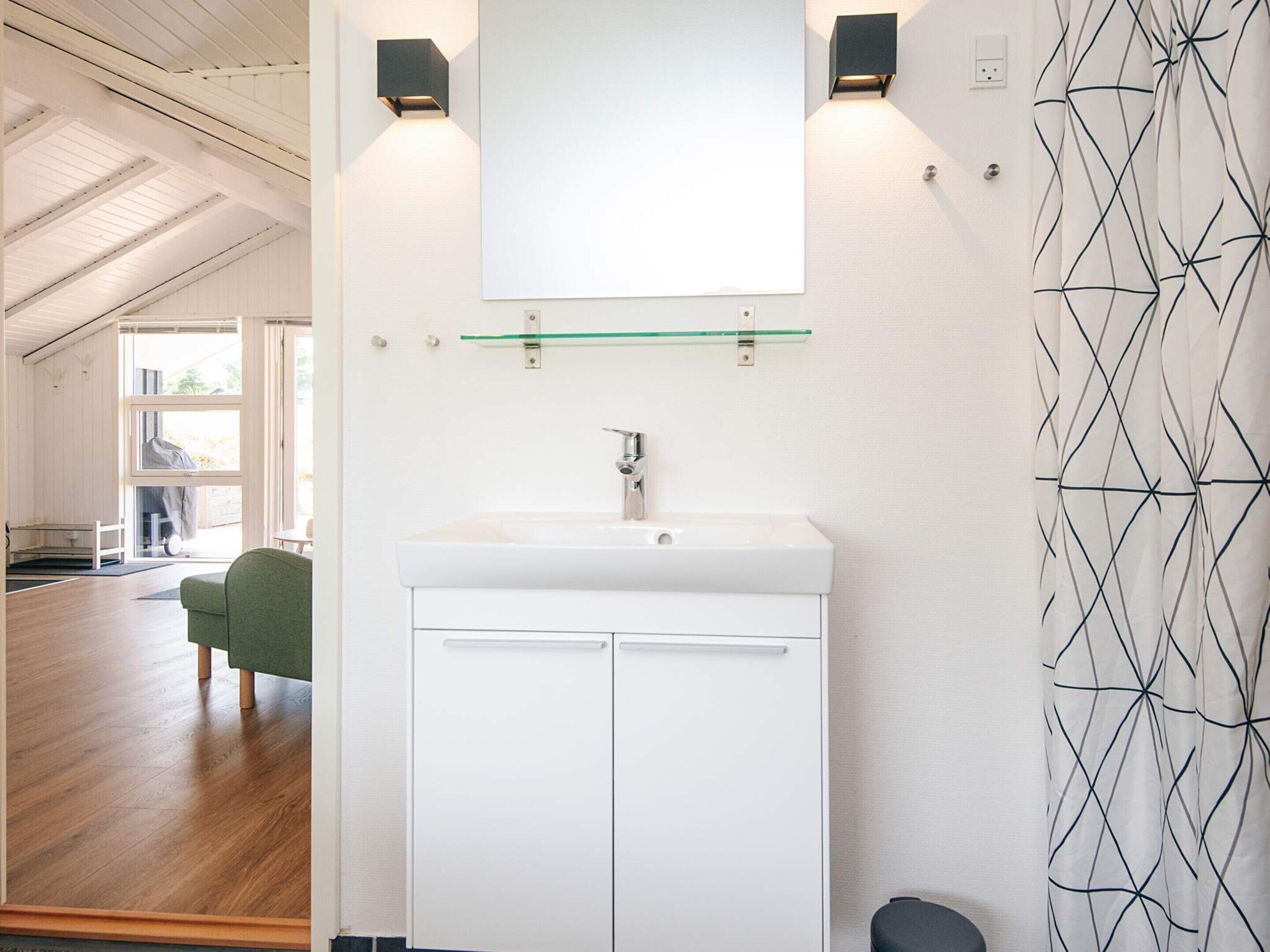 Un baño moderno con un lavamanos blanco, un espejo encima y dos luces empotradas.