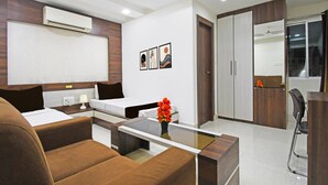A modern hotel room with a bed, a sofa, a coffee table, a desk, and a wardrobe. - Deluxe With Twin Bed Hotel Amrit Plaza (Dhanbad)