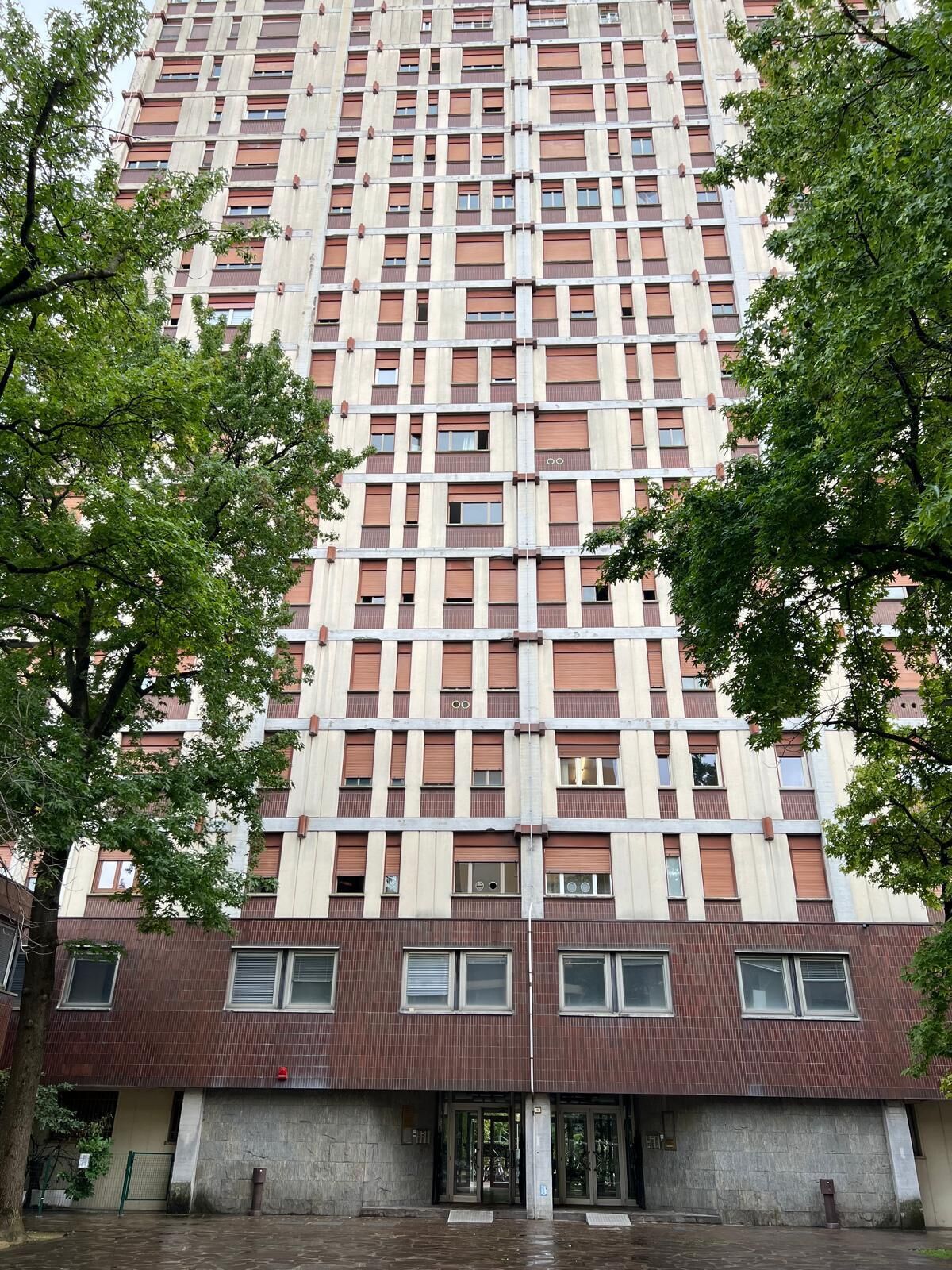 Ein Hochhaus mit einem Raster aus Fenstern und Balkonen, das eine zentrale Eingangstür aus Glas hat.