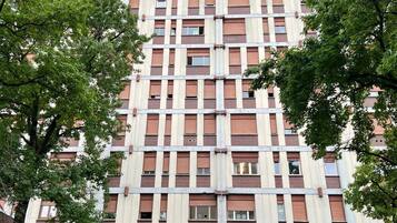 Ein Hochhaus mit einem Raster aus Fenstern und Balkonen, das eine zentrale Eingangstür aus Glas hat.